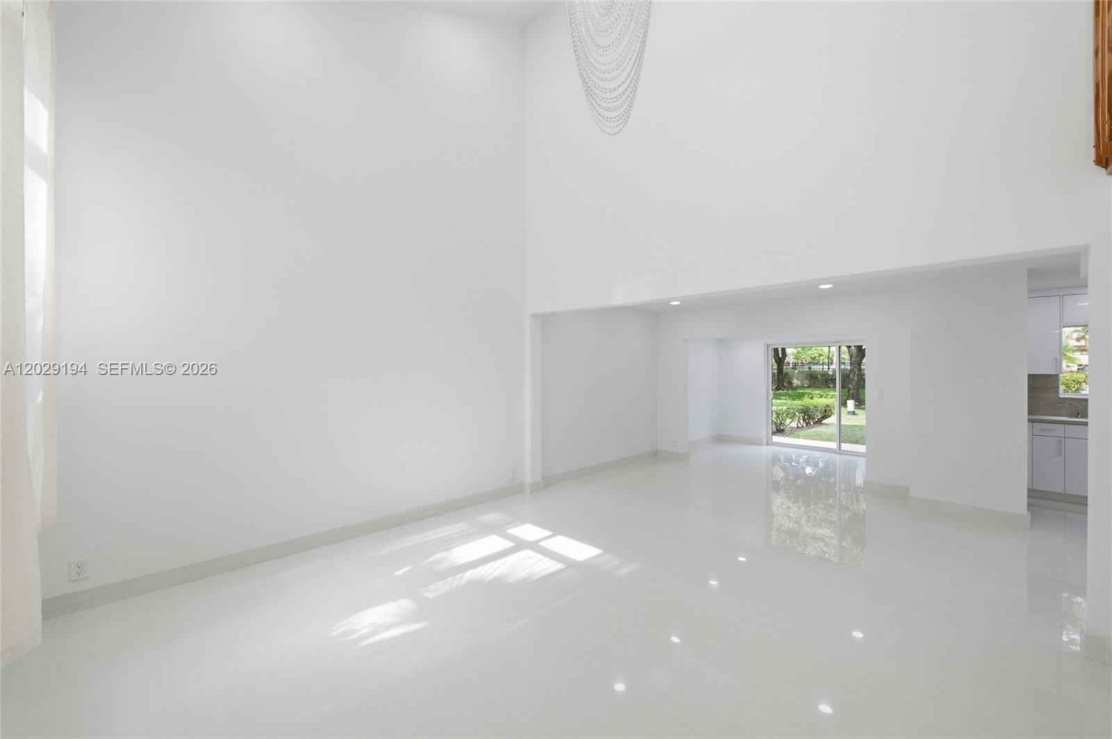 A bright, minimalist living room features high ceilings, white tile floors, and a sliding glass door — 22384 Thousand Pines Ln, Boca Raton FL 33428, BOCA RATON, FL