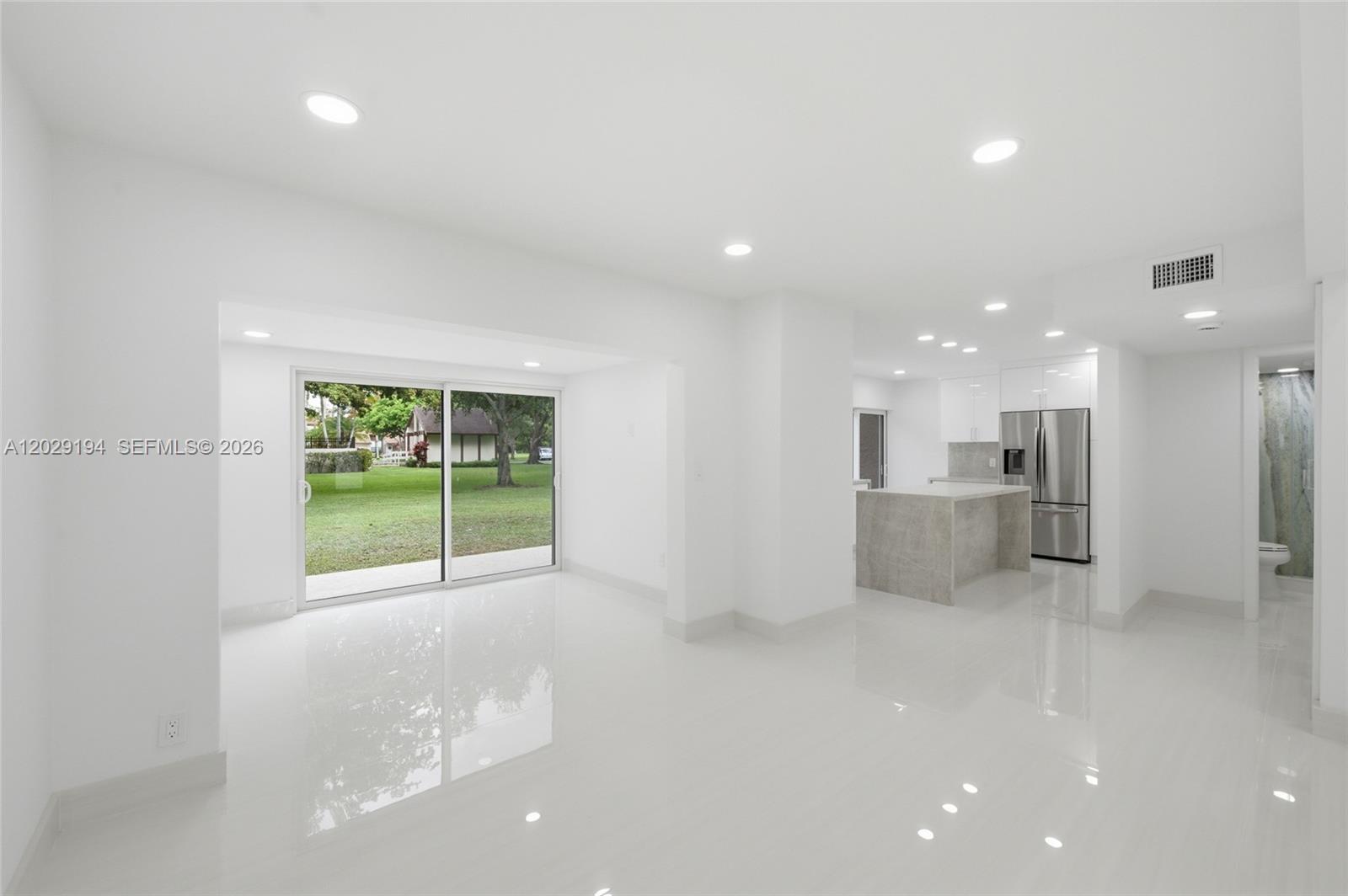 A bright, open-concept living area with white tile floors, recessed lighting, and a modern kitchen — 22384 Thousand Pines Ln, Boca Raton FL 33428, BOCA RATON, FL