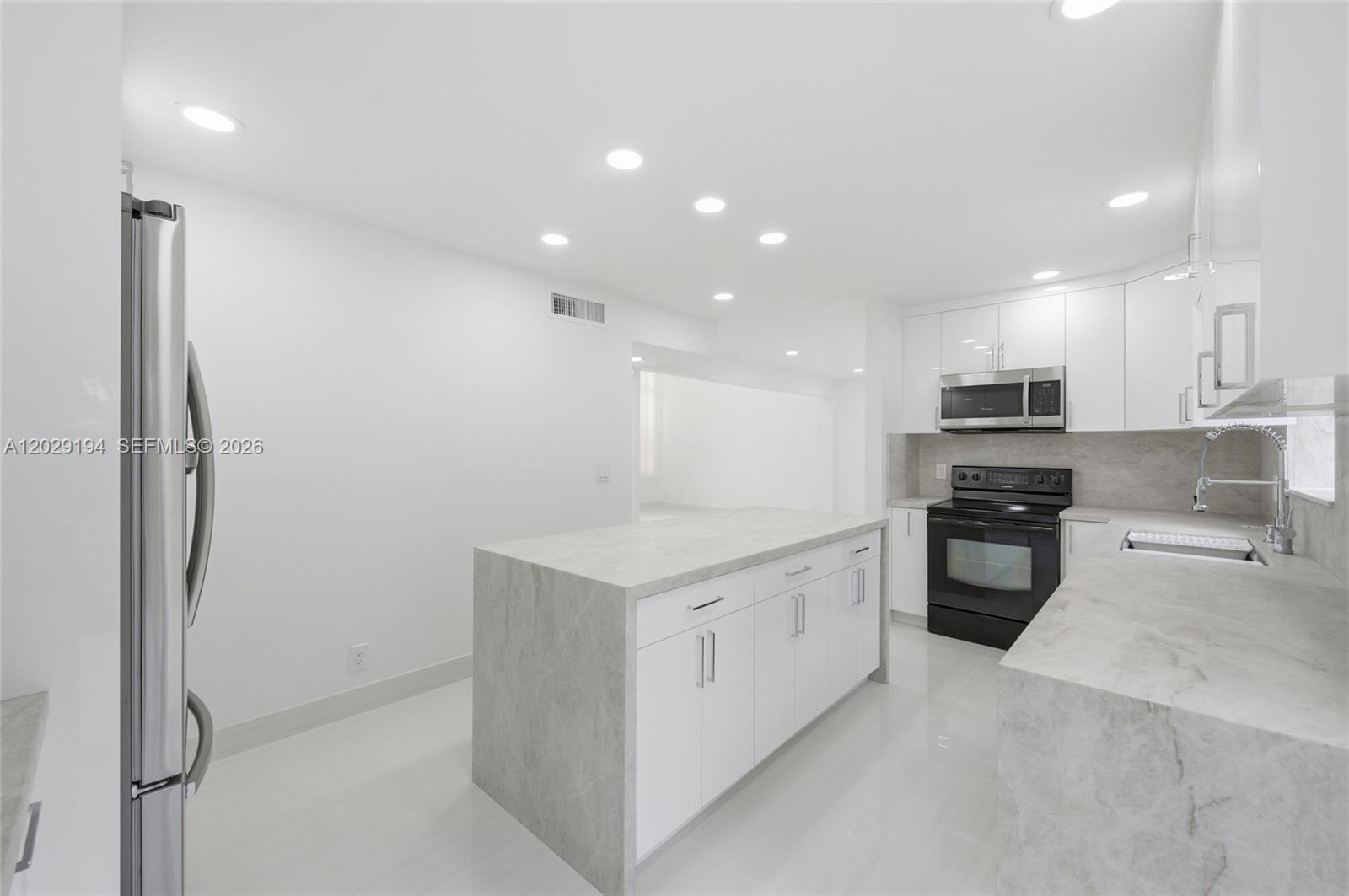 A modern kitchen features white cabinetry, marble-patterned countertops, and stainless steel appliances — 22384 Thousand Pines Ln, Boca Raton FL 33428, BOCA RATON, FL