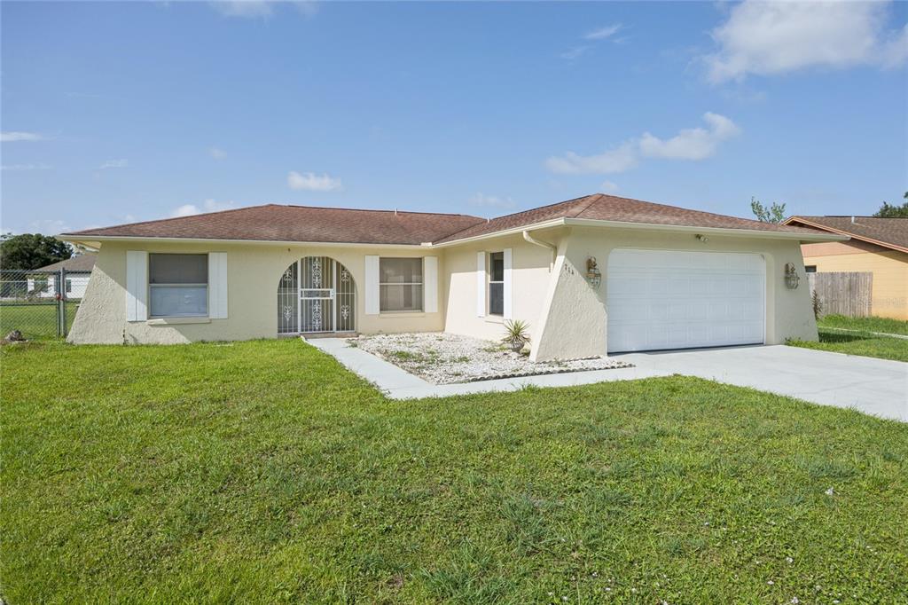 A single-story house with a white stucco exterior, a two-car garage, and a front lawn — 714 TOURNAMENT LANE, KISSIMMEE, FL