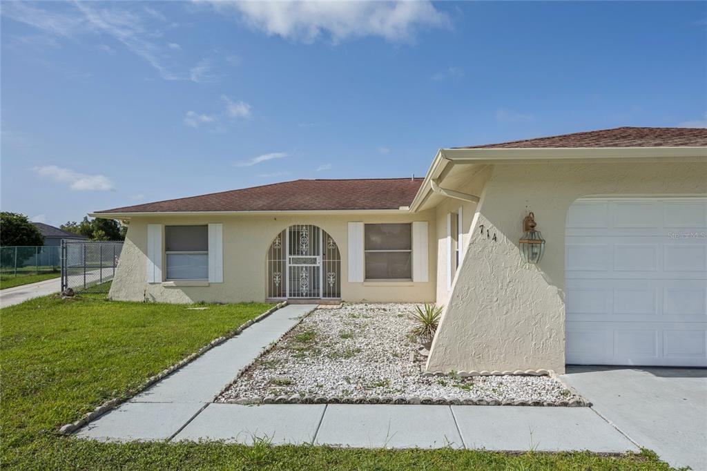 A single-story house with a white stucco exterior, a gravel front yard, and a garage — 714 TOURNAMENT LANE, KISSIMMEE, FL