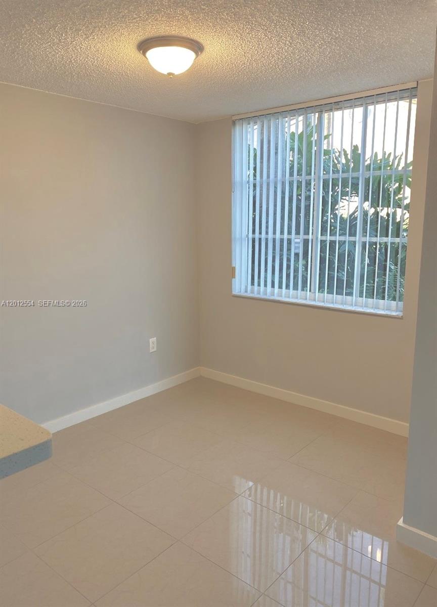 An empty room features light-colored tile flooring, gray walls, and a window with vertical blinds — 12118 Saint Andrews Pl # 107, Miramar FL 33025, MIRAMAR, FL