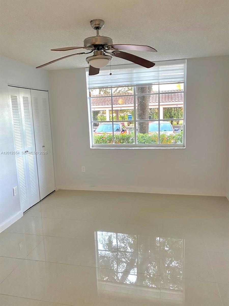 A bedroom features white tile floors, a ceiling fan, a closet, and a large window — 12118 Saint Andrews Pl # 107, Miramar FL 33025, MIRAMAR, FL