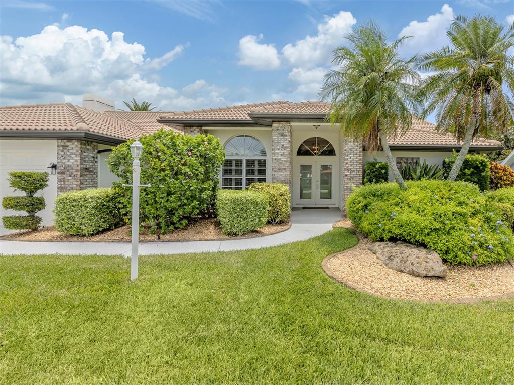 The exterior of a single-story house features a brick facade, tile roof, and palm trees — 1428 GLENEAGLES DRIVE, VENICE, FL