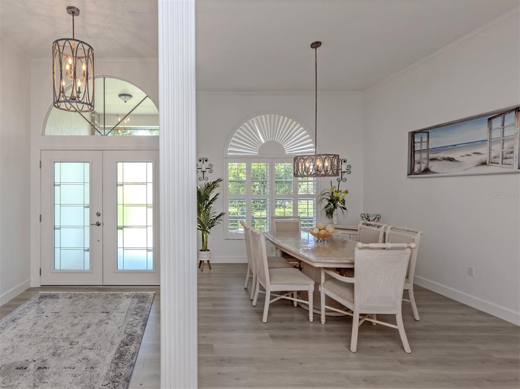A dining room with a stone-topped table and light wood flooring sits near an entryway — 1428 GLENEAGLES DRIVE, VENICE, FL
