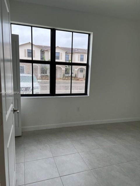 An empty room with light-colored tile flooring and a large window overlooking suburban homes — 12989 SW 233rd Ter # 12989, Miami FL 33032, MIAMI, FL