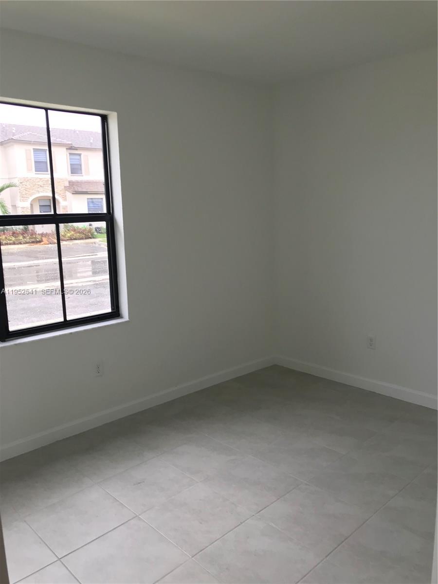 An empty room with white walls, light tile flooring, and a window overlooking a street — 12989 SW 233rd Ter # 12989, Miami FL 33032, MIAMI, FL
