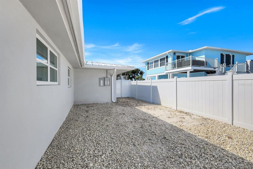 A side yard with gravel ground cover, a white vinyl fence, and a white house — 7987 ESTERO BOULEVARD, FORT MYERS BEACH, FL