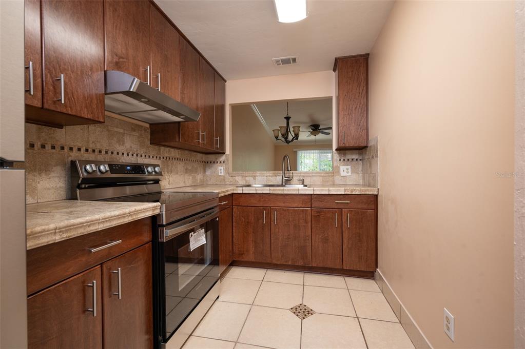 A kitchen features dark wood cabinets, tile countertops, stainless steel appliances, and light floor tiles — 3409 NW 52ND TERRACE, GAINESVILLE, FL