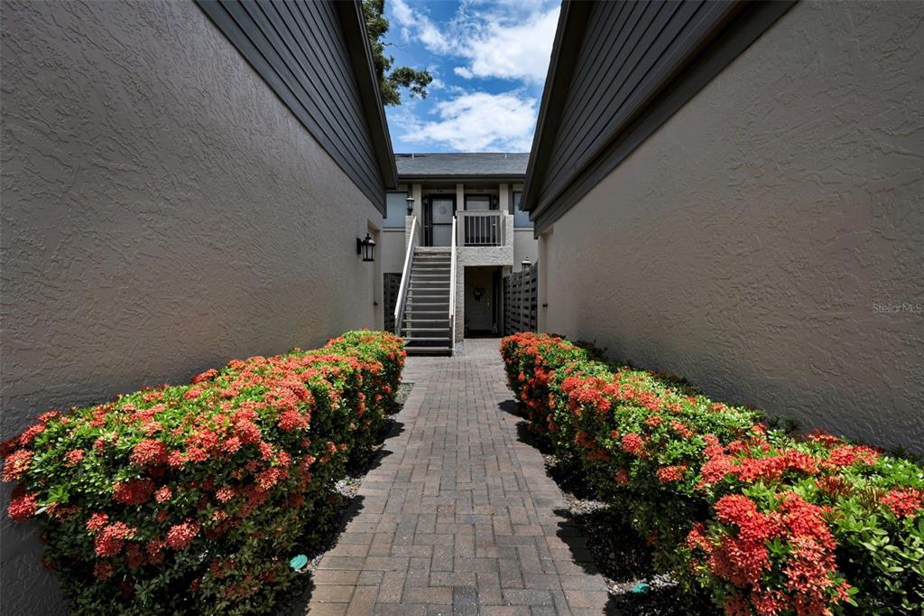 A brick walkway leads between two stucco buildings toward an outdoor staircase and entrance — 3165 LANDMARK DRIVE UNIT 711, CLEARWATER, FL