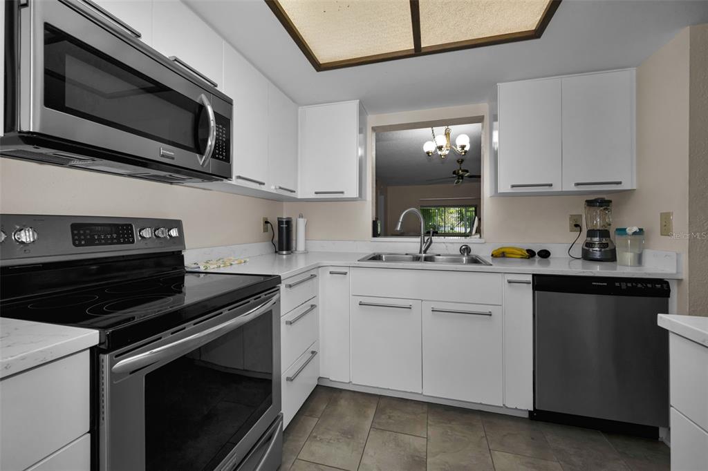 A kitchen features white cabinets, stainless steel appliances, and a pass-through window to another room — 3165 LANDMARK DRIVE UNIT 711, CLEARWATER, FL