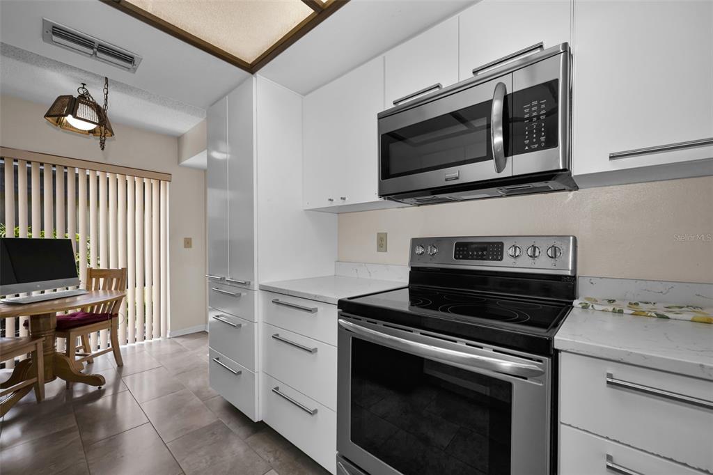 A kitchen features white cabinets, stainless steel appliances, and a dining area with a table — 3165 LANDMARK DRIVE UNIT 711, CLEARWATER, FL