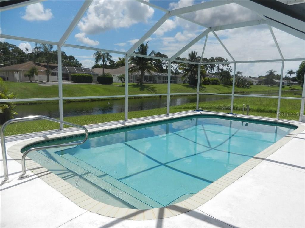A screened-in swimming pool overlooks a canal and neighboring houses on a sunny day — 80 MARINER LANE, ROTONDA WEST, FL