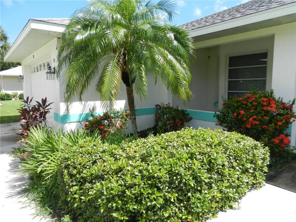 A palm tree and manicured shrubs sit in front of a white house with teal trim — 80 MARINER LANE, ROTONDA WEST, FL
