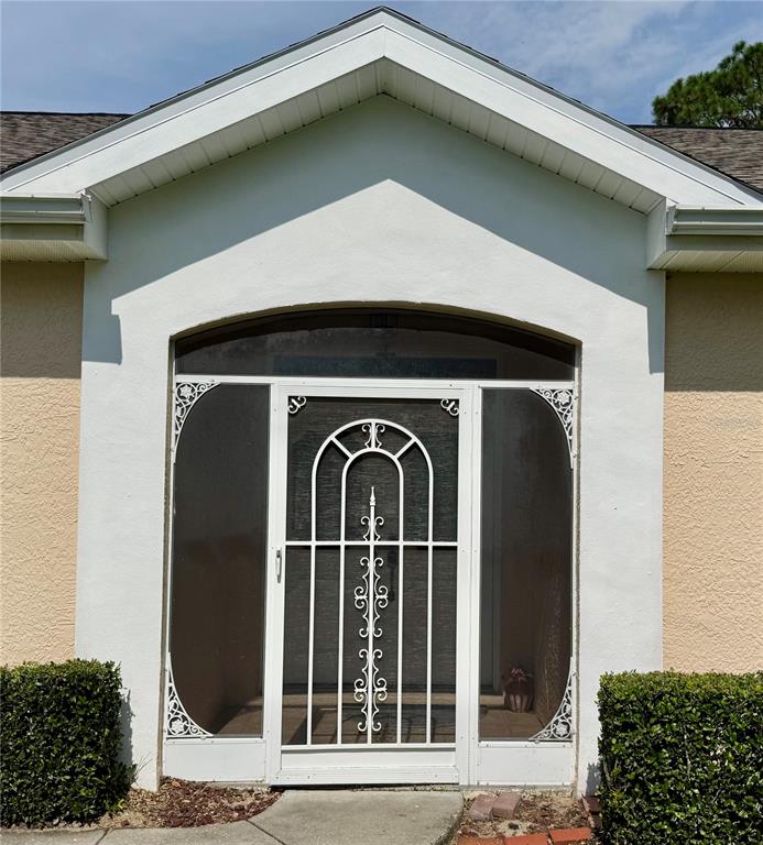 The exterior of a home features a white arched front door with decorative metal screen — 5688 LEGEND HILLS LANE, SPRING HILL, FL