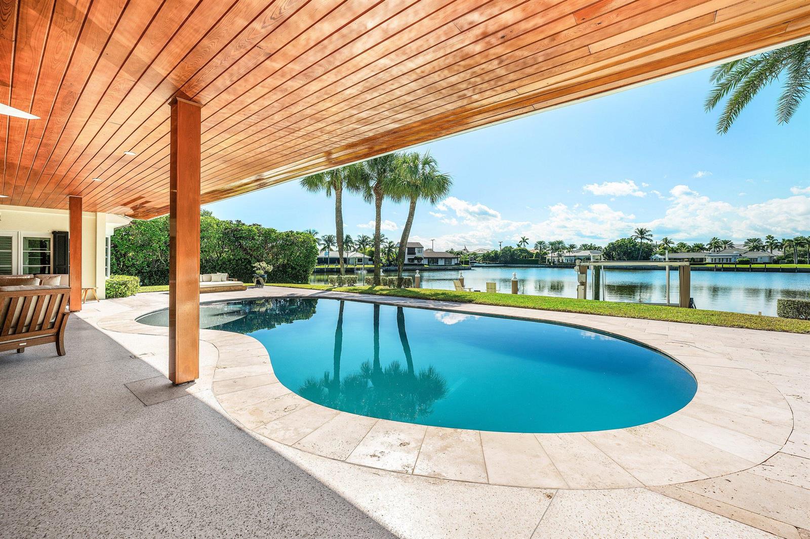 A covered patio with a wood ceiling overlooks a swimming pool and a waterfront canal — 50 Spoonbill Road, Manalapan FL 33462, MANALAPAN, FL