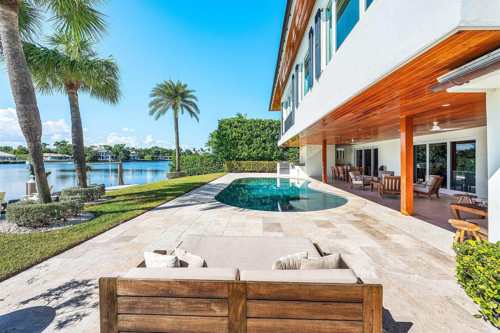 A patio with a pool, lounge furniture, and a wooden ceiling overlooks a waterfront canal — 50 Spoonbill Road, Manalapan FL 33462, MANALAPAN, FL