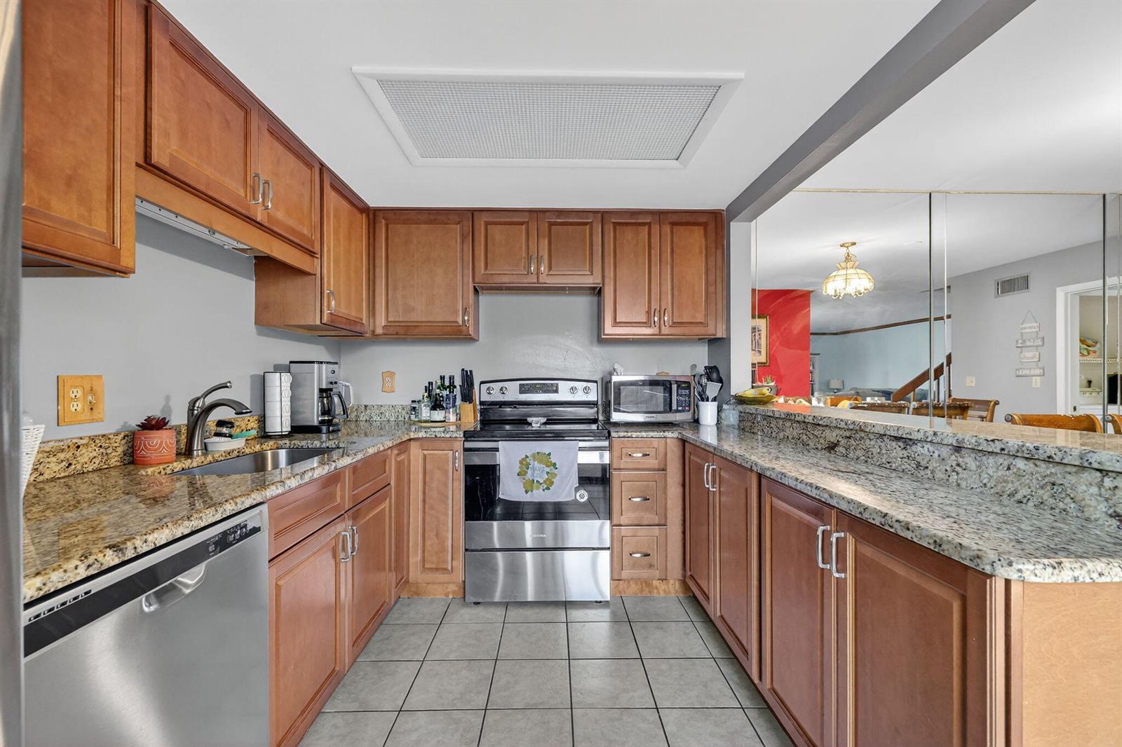A kitchen features wood cabinets, granite countertops, stainless steel appliances, and gray tile flooring — 3860 Jefferson Street, Stuart FL 34997, STUART, FL