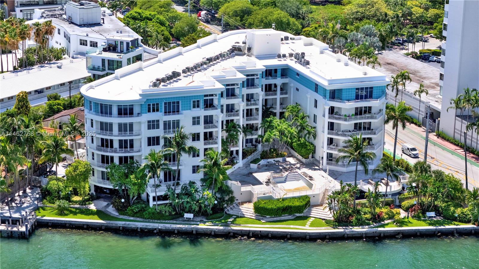 An aerial view shows a multi-story white apartment building with balconies overlooking a waterfront pool — 1 Century Ln # 209, Miami Beach FL 33139, MIAMI BEACH, FL