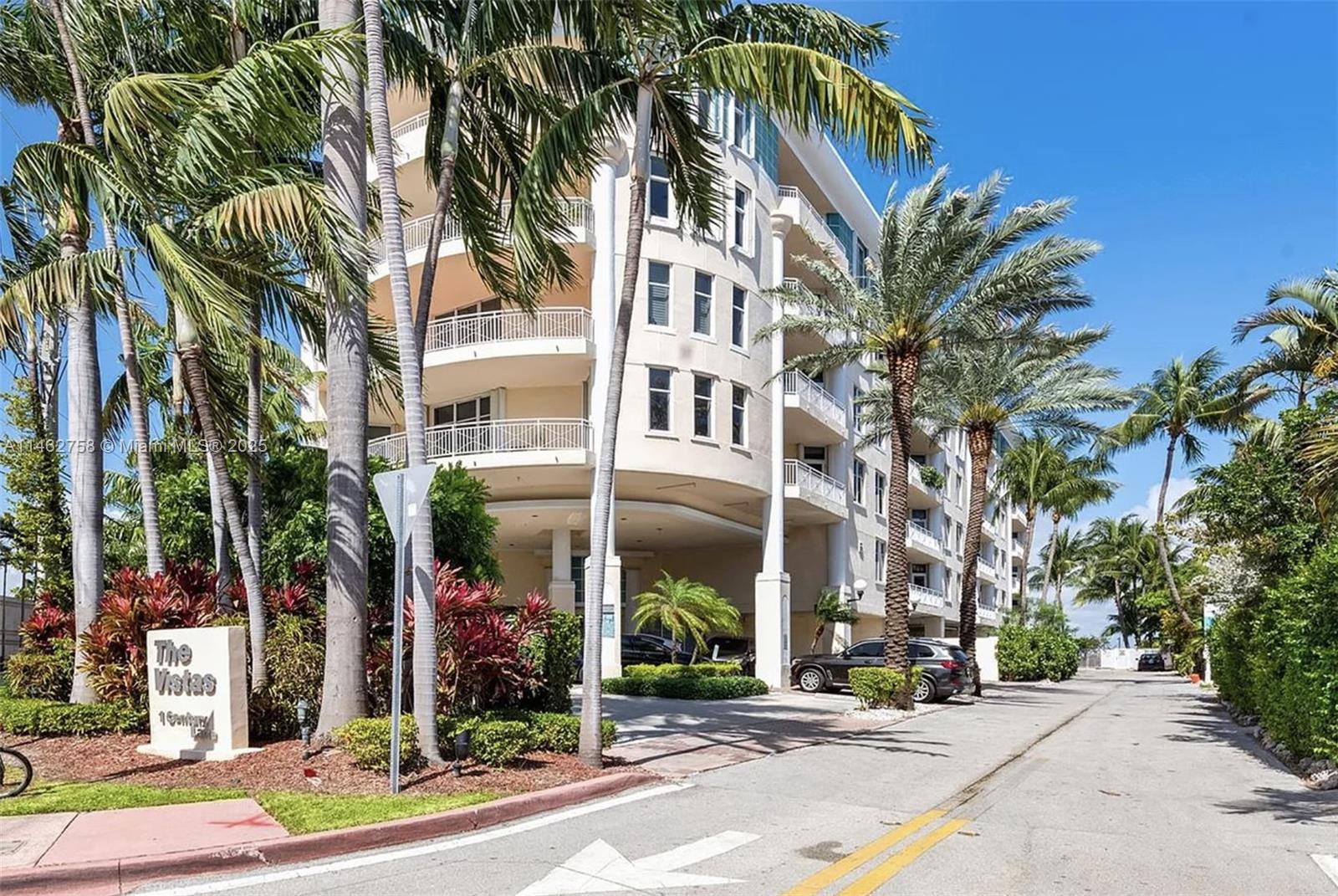 The exterior of a multi-story residential building features curved balconies and surrounding palm trees — 1 Century Ln # 209, Miami Beach FL 33139, MIAMI BEACH, FL