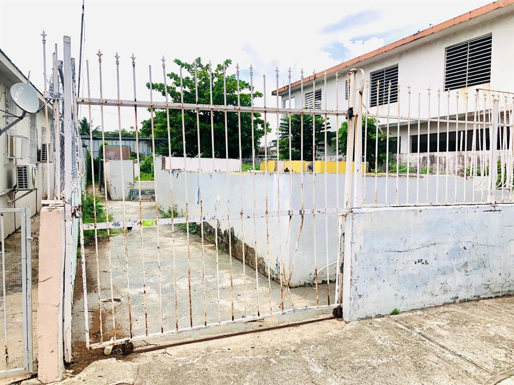 A white metal gate opens to a concrete driveway leading toward a low-walled outdoor space — 225 RUÍZ BELVIS, SAN JUAN, PR