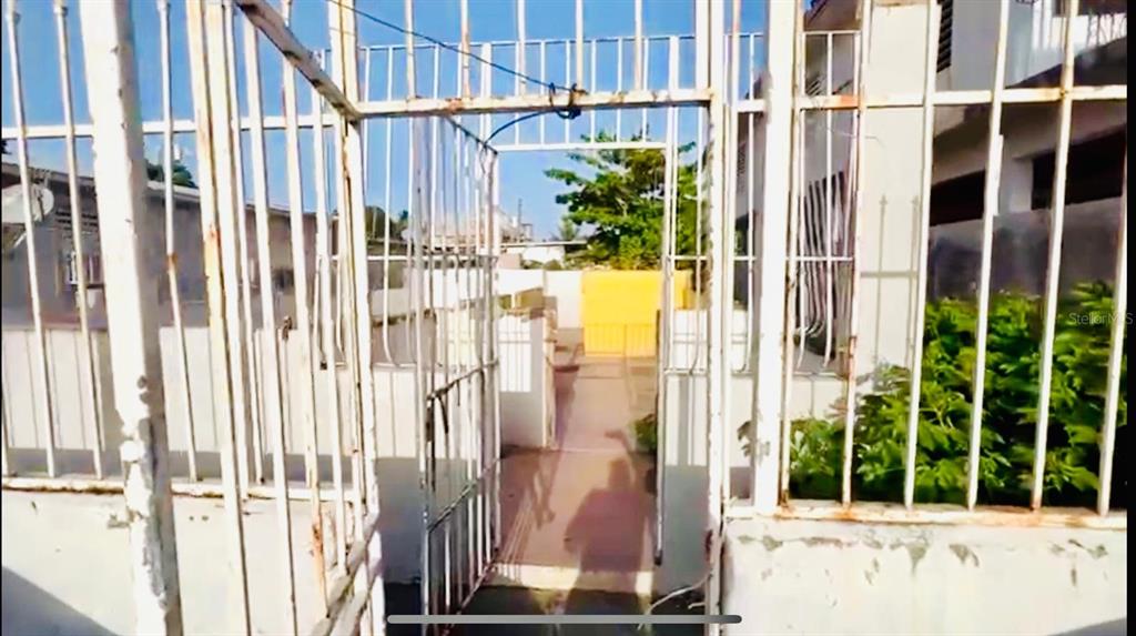 A white metal gate opens to a paved walkway leading toward a yellow exterior wall — 225 RUÍZ BELVIS, SAN JUAN, PR