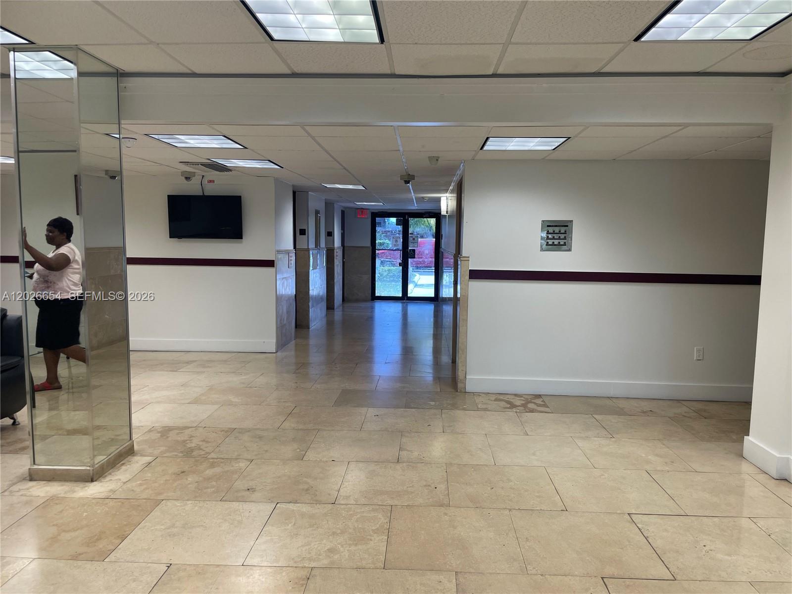A tiled hallway features a mirrored pillar, a wall-mounted television, and glass double doors — 4174 Inverrary Dr # 903, Lauderhill FL 33319, LAUDERHILL, FL