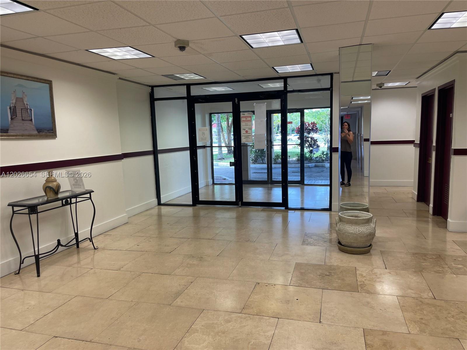 A lobby features a tiled floor, glass entrance doors, a console table, and a mirror — 4174 Inverrary Dr # 903, Lauderhill FL 33319, LAUDERHILL, FL