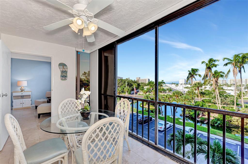 A sunroom with a glass-topped table, wicker chairs, and a view of palm trees outside — 5855 MIDNIGHT PASS ROAD UNIT 426, SARASOTA, FL