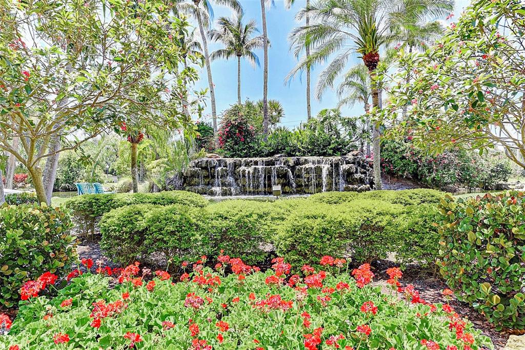 A stone waterfall feature sits behind a lush garden with red flowers and palm trees — 5855 MIDNIGHT PASS ROAD UNIT 426, SARASOTA, FL