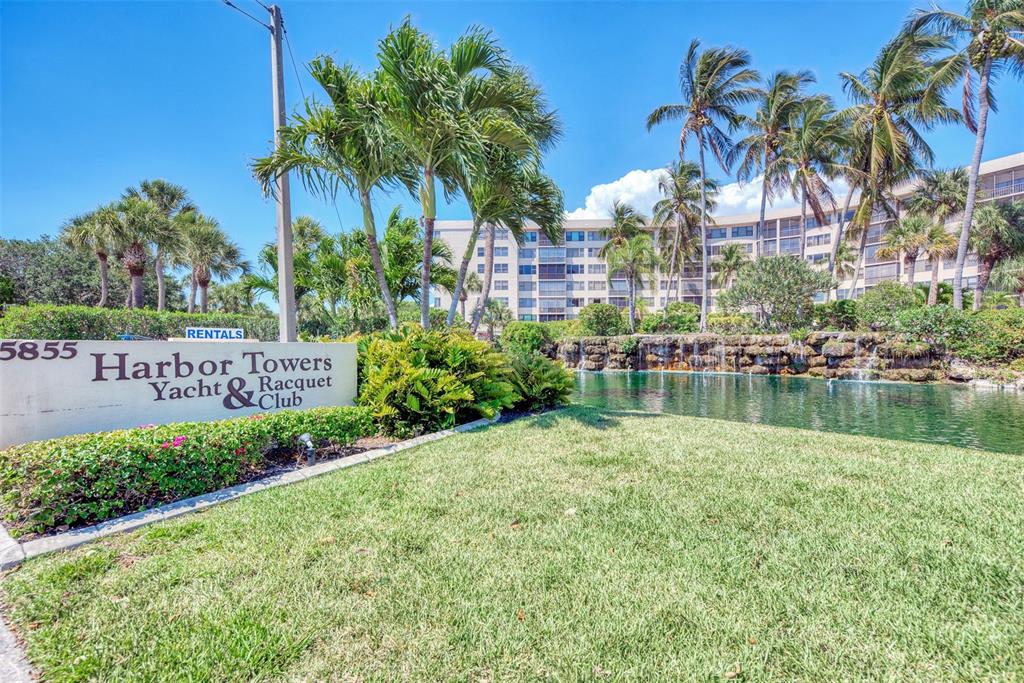 A sign for Harbor Towers Yacht & Racquet Club stands before a pond and building — 5855 MIDNIGHT PASS ROAD UNIT 426, SARASOTA, FL