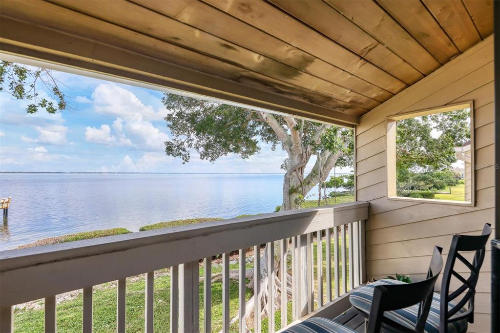 A covered wooden balcony overlooks a large body of water with a tree nearby — 5270 GULF OF MEXICO DRIVE UNIT 508, LONGBOAT KEY, FL