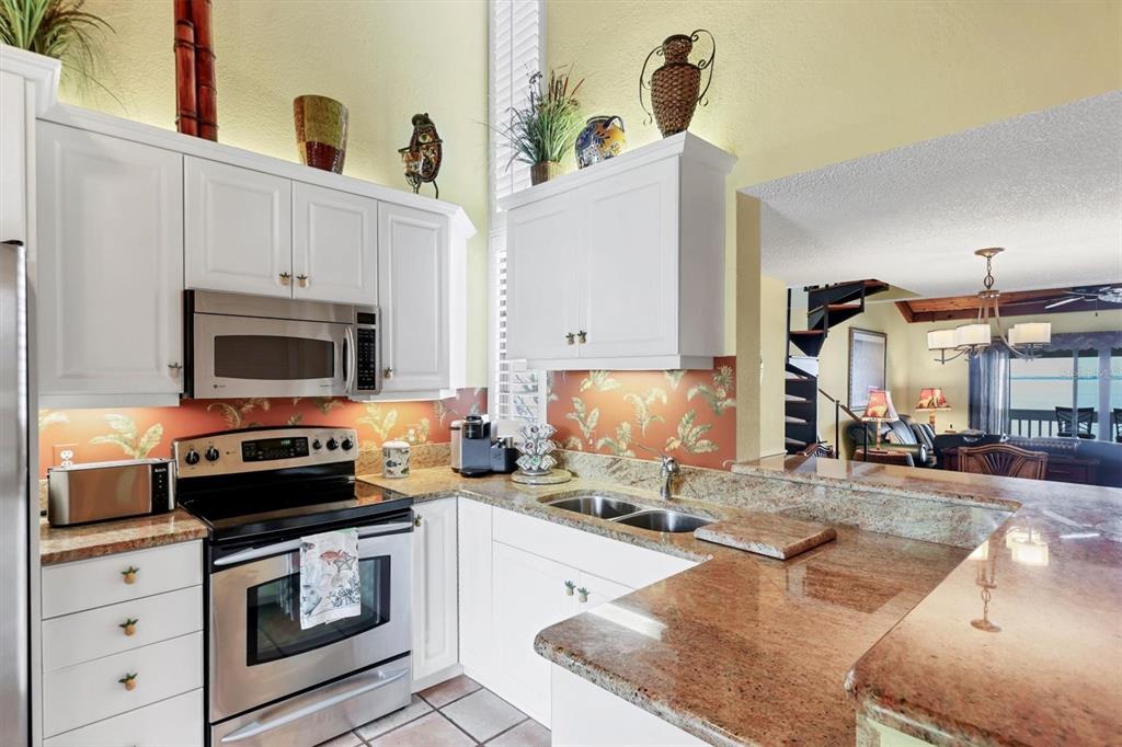 A kitchen features white cabinets, granite countertops, stainless steel appliances, and a tropical-patterned backsplash — 5270 GULF OF MEXICO DRIVE UNIT 508, LONGBOAT KEY, FL