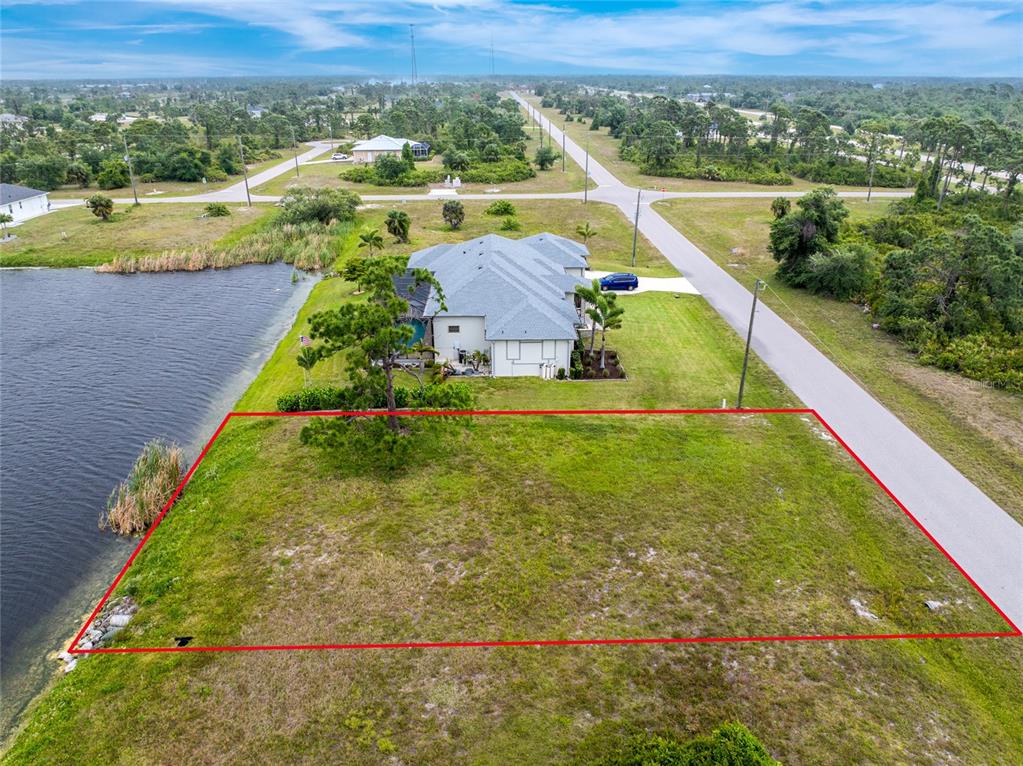 An aerial view shows a vacant, rectangular waterfront lot outlined in red next to a house — 70 BRIG CIRCLE E, PLACIDA, FL