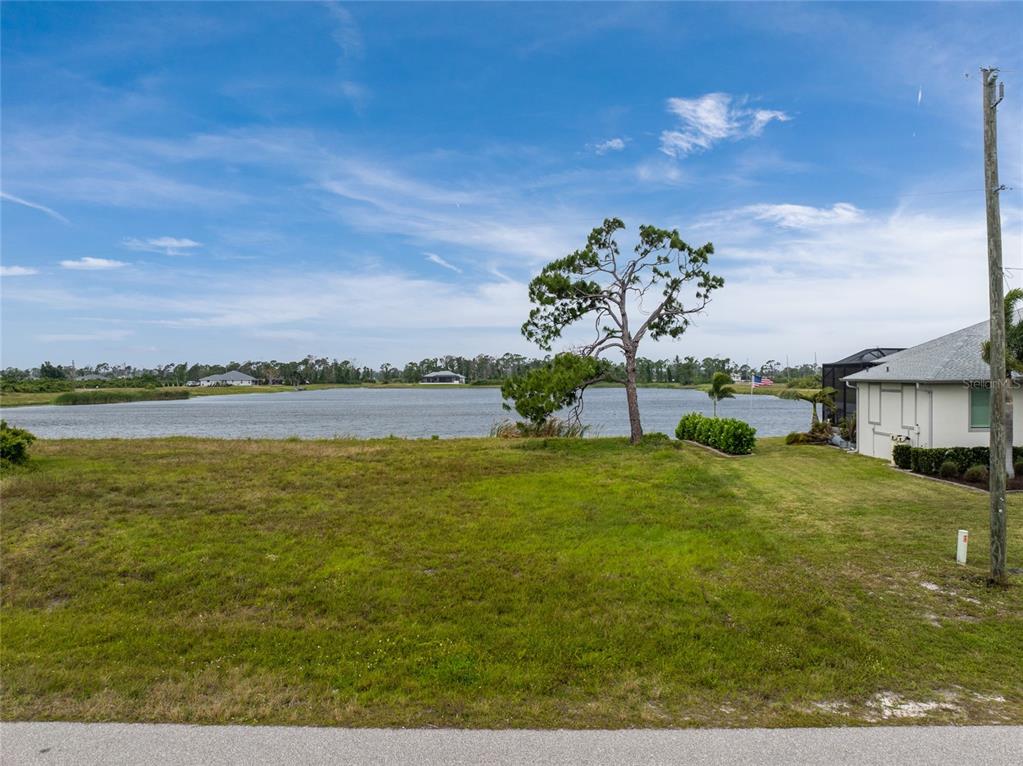 A grassy vacant lot overlooks a lake with a single tree and neighboring house — 70 BRIG CIRCLE E, PLACIDA, FL