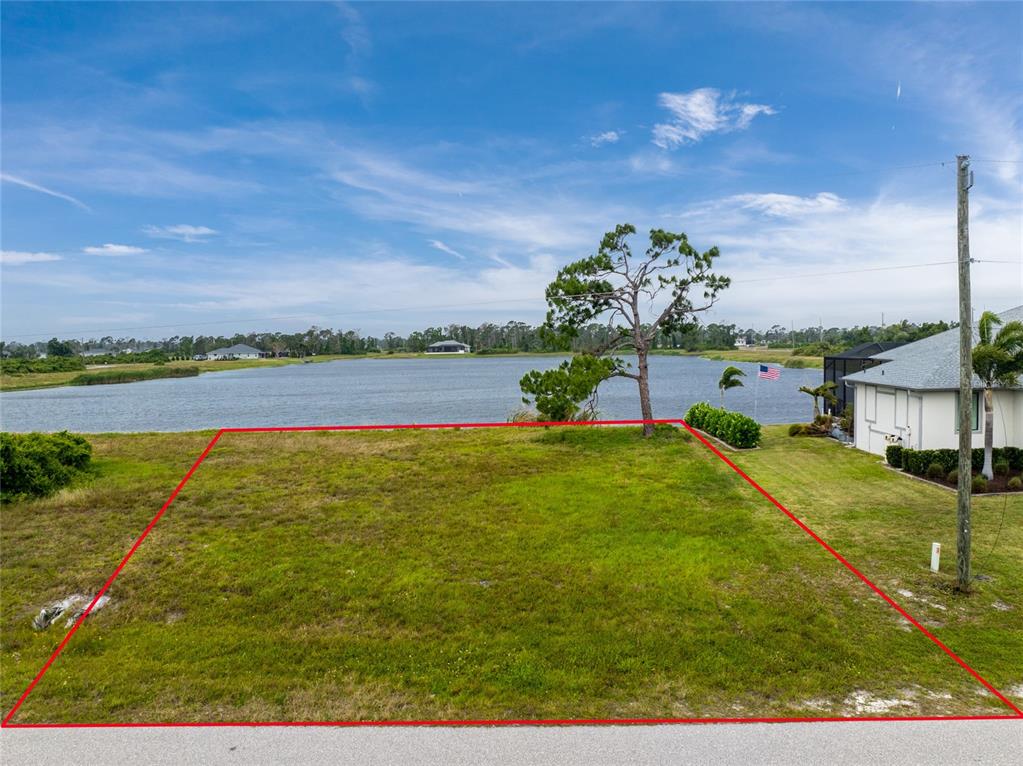 An elevated view of a vacant, grassy waterfront lot outlined in red — 70 BRIG CIRCLE E, PLACIDA, FL