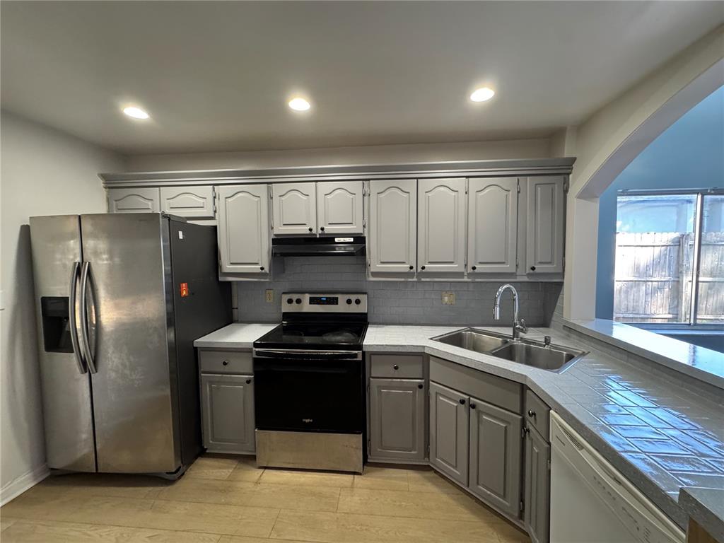 A kitchen features gray cabinets, stainless steel appliances, tiled countertops, and light wood-look flooring — 7237 HARBOR HEIGHTS CIRCLE, ORLANDO, FL