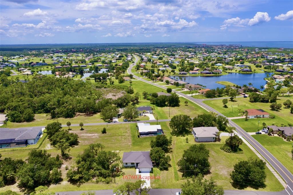 An aerial view shows a residential neighborhood with houses, green lawns, and a large lake — 16760 ACAPULCO ROAD, PUNTA GORDA, FL