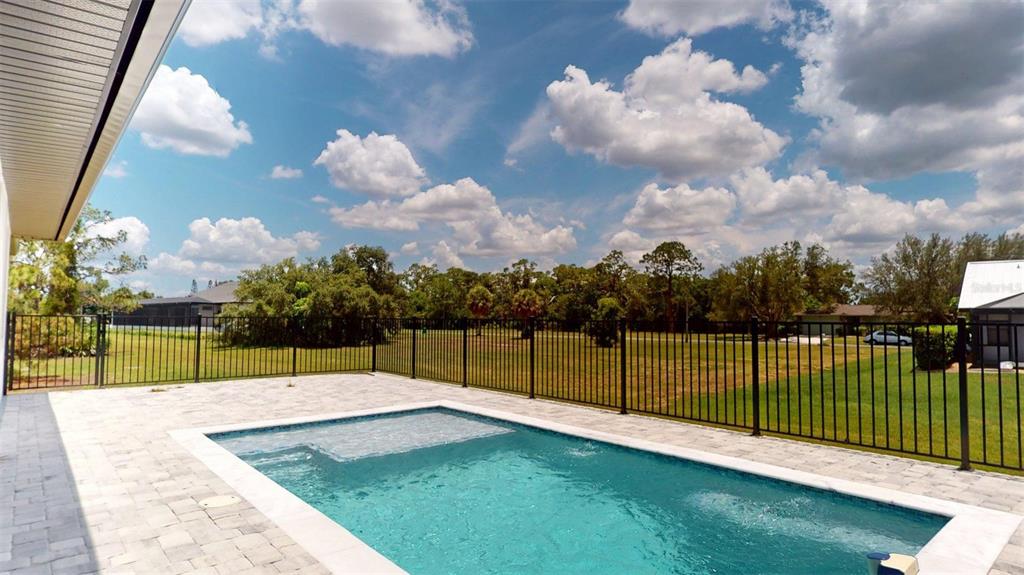 A backyard swimming pool with a paved deck and black metal fencing under a cloudy sky — 16760 ACAPULCO ROAD, PUNTA GORDA, FL