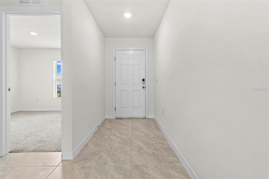 An entryway with light tile flooring leads to a white front door and a room — 10306 SE 161ST LANE ROAD, SUMMERFIELD, FL