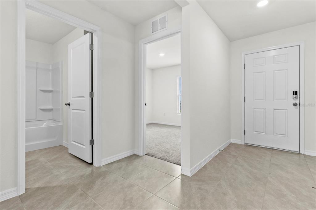 A tiled entryway features a white front door, a bathroom doorway, and a carpeted bedroom — 10306 SE 161ST LANE ROAD, SUMMERFIELD, FL