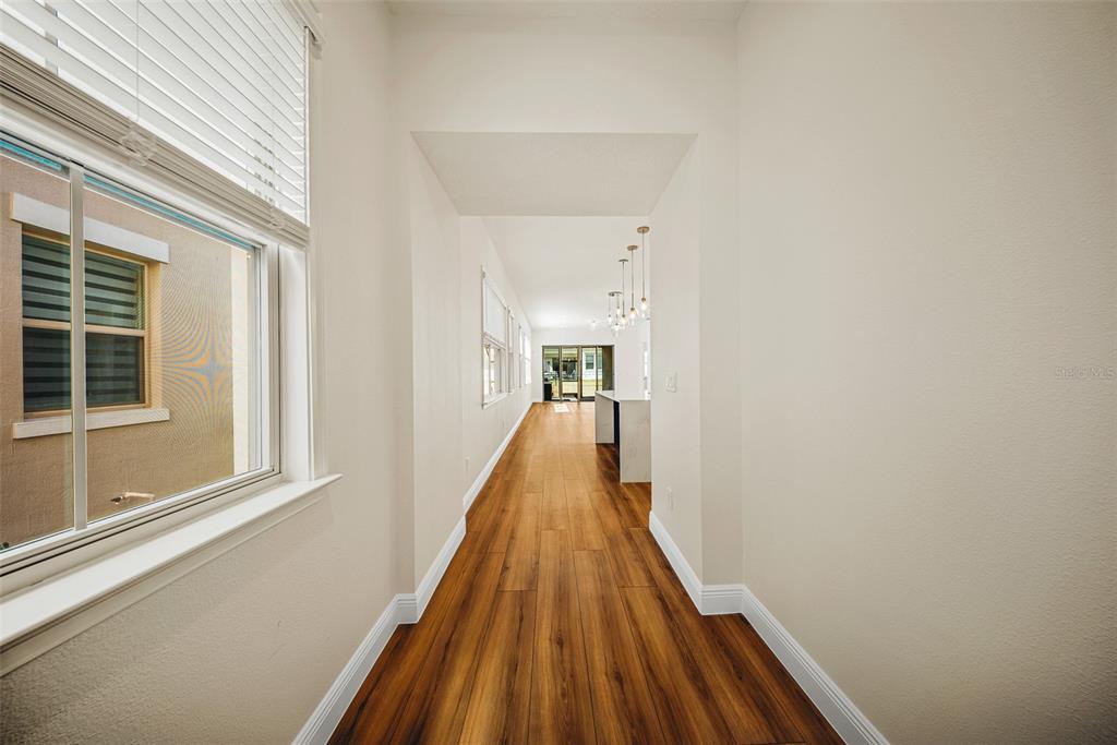 A long hallway with wood-look flooring leads toward a kitchen with a central island — 13315 CAMBORNE PLACE, ORLANDO, FL