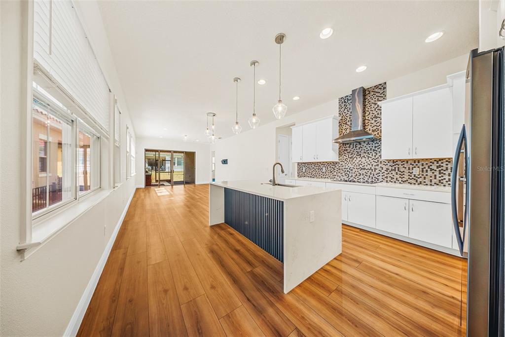 A modern kitchen features white cabinetry, a blue-paneled island, and wood-look flooring — 13315 CAMBORNE PLACE, ORLANDO, FL