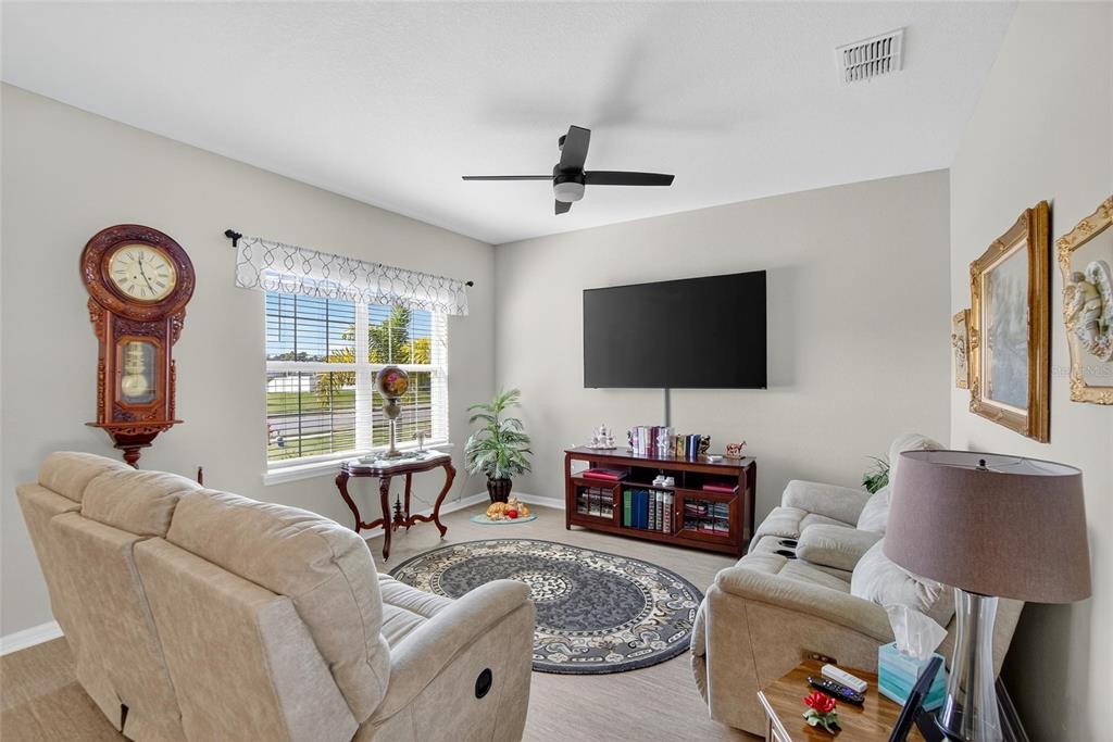 A living room features a television, two beige sofas, a grandfather clock, and a rug — 6852 MOSSY OAK LANE, LAKELAND, FL