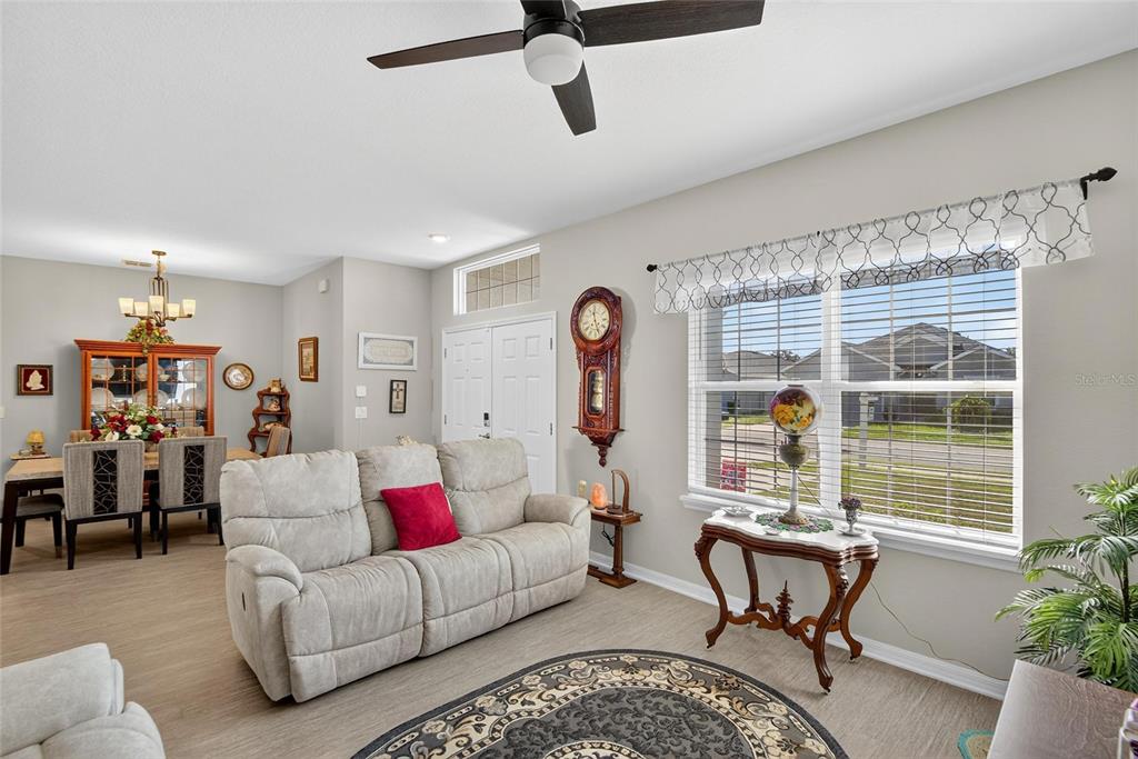 A living room with a beige sofa, a grandfather clock, and an adjacent dining area — 6852 MOSSY OAK LANE, LAKELAND, FL