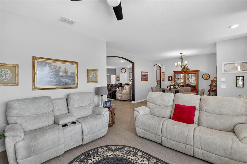A living room features two light-colored reclining sofas, a circular rug, and an arched entryway — 6852 MOSSY OAK LANE, LAKELAND, FL