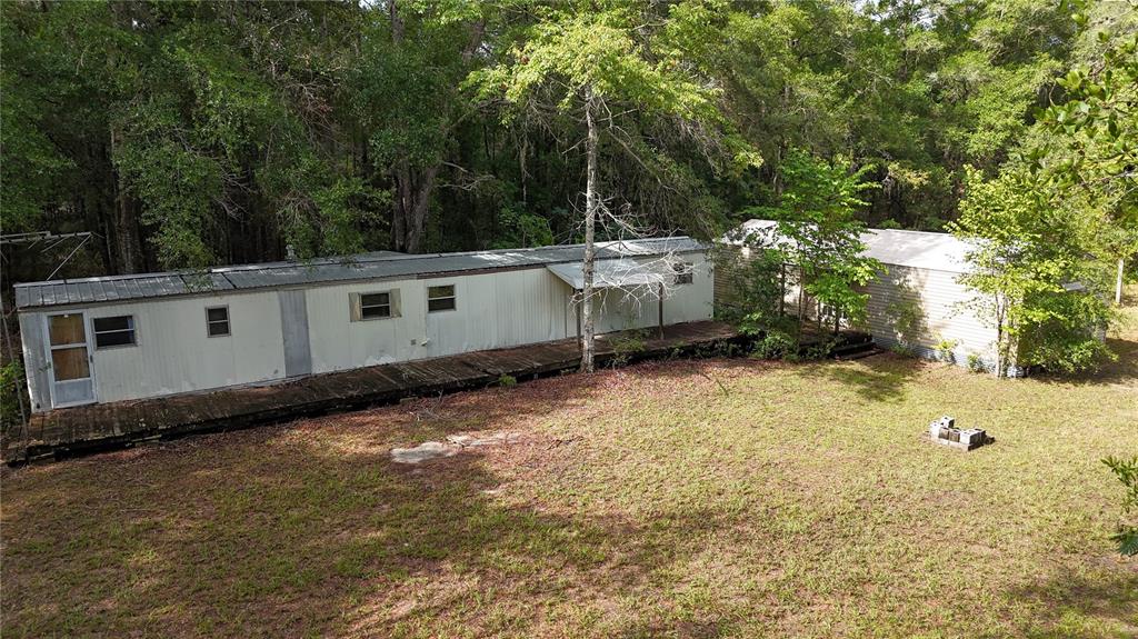 An aerial view shows two mobile homes connected by a wooden deck in a wooded area — 9730 NE STATE ROAD 24, ARCHER, FL