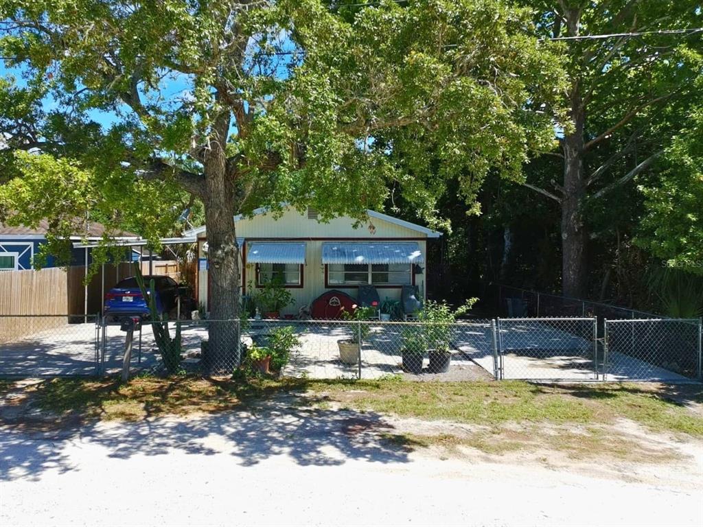 A single-story house with a fenced yard, paved driveway, and large trees in front — 7101 JEANNE AVENUE, HUDSON, FL