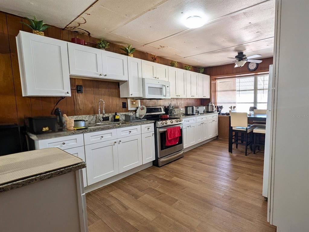 A kitchen features white cabinets, wood-paneled walls, stainless steel appliances, and wood-look flooring — 7101 JEANNE AVENUE, HUDSON, FL