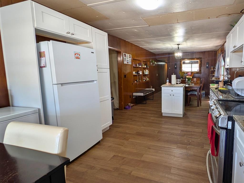 A kitchen with white cabinets, a white refrigerator, and wood-paneled walls leads to a dining area — 7101 JEANNE AVENUE, HUDSON, FL